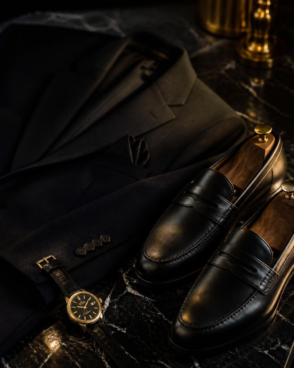 Tailored blazer, black leather loafers and gold watch on black marble